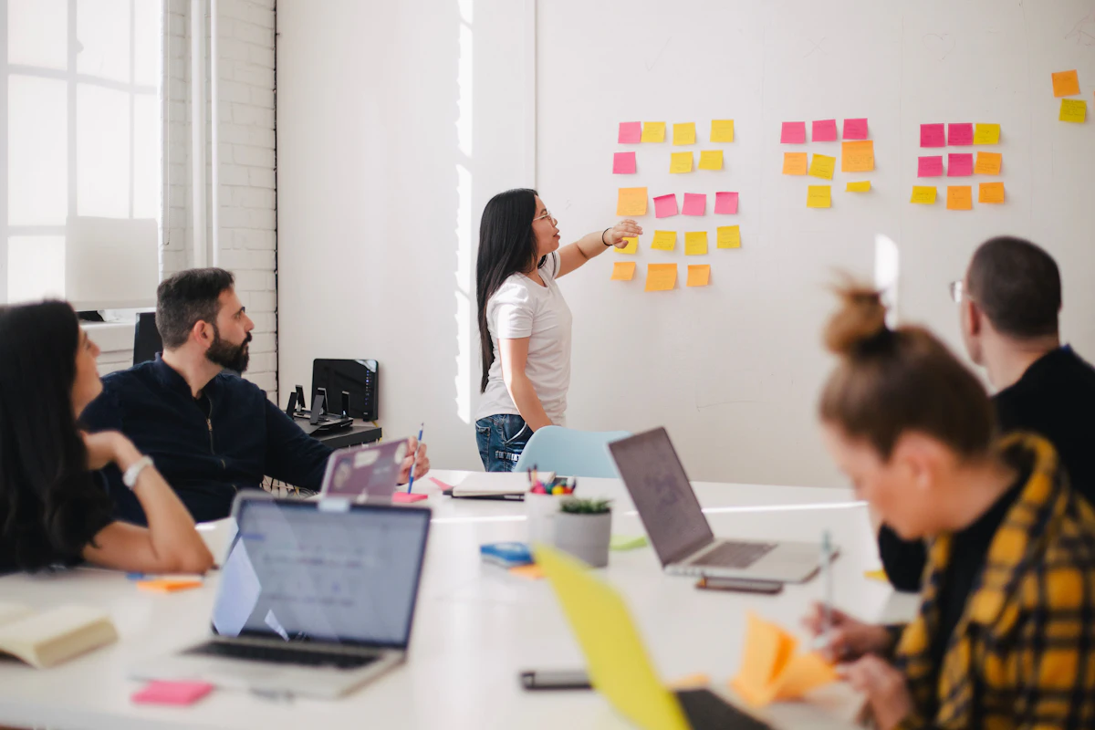 A team mapping out a project on a wall of sticky notes, laptops open around the table
