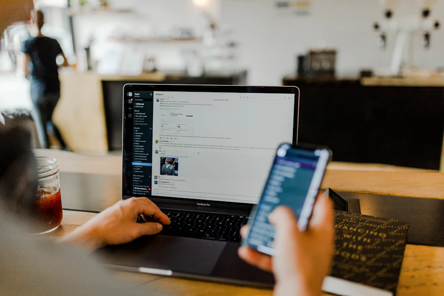 Someone reading messages on a laptop while holding a phone